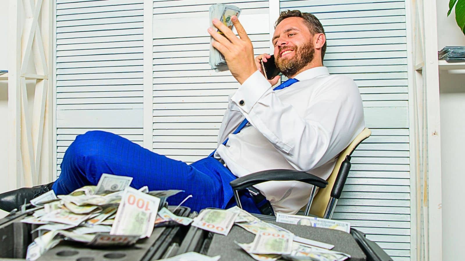Greedy businessman sitting in a chair on the phone with cash all around him