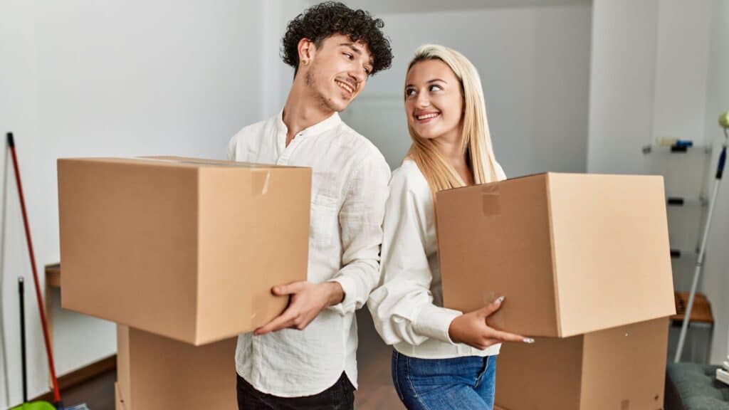 Young couple holding moving boxes and smiling at each other