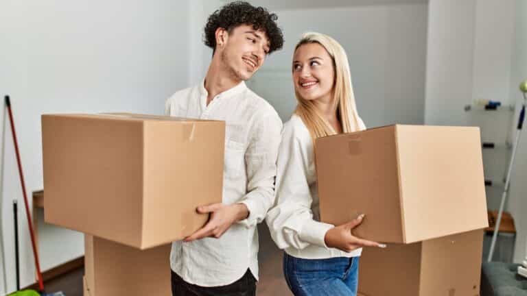 Young couple holding moving boxes and smiling at each other