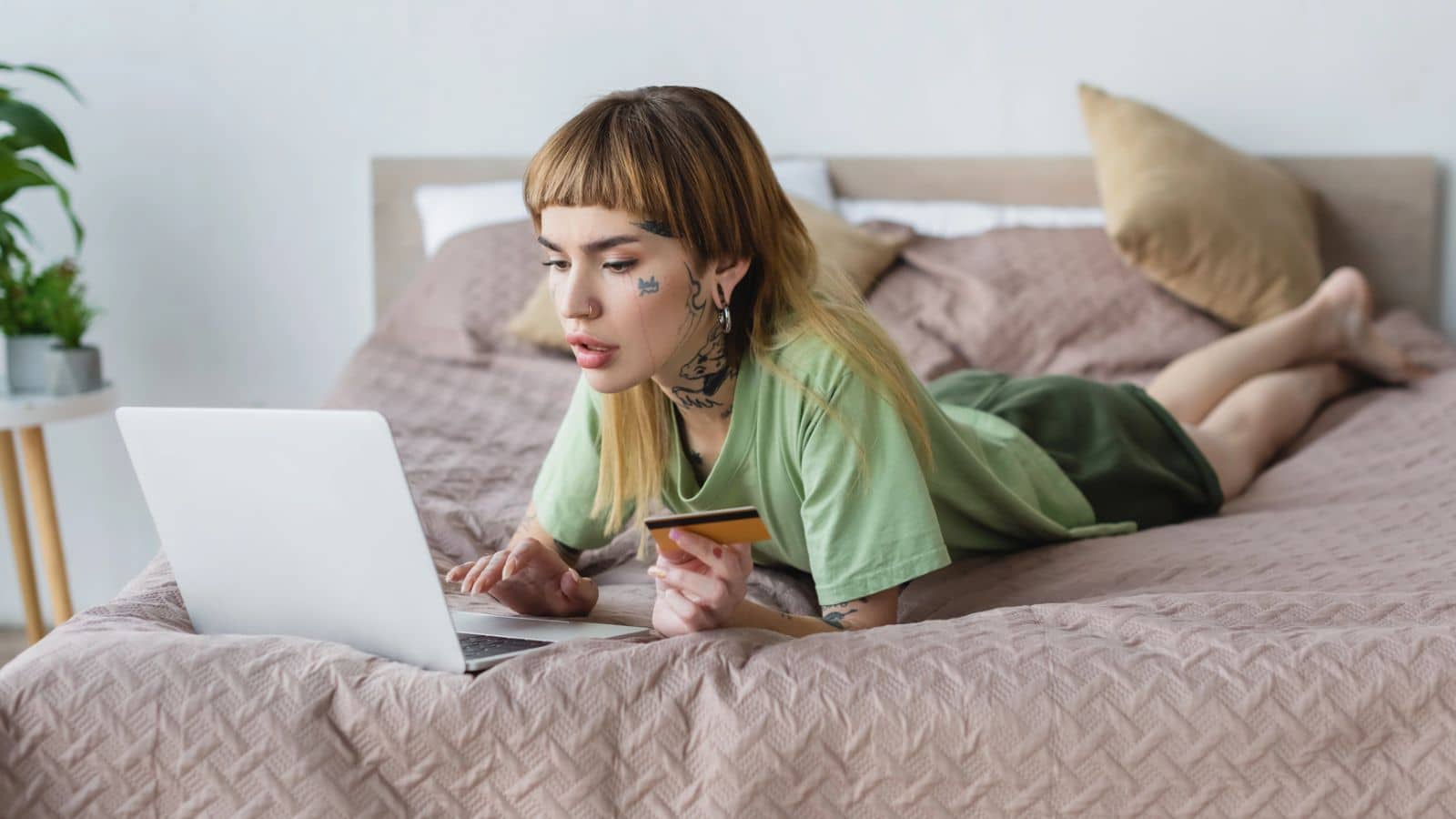 Gen Z woman laying on a bed shopping on her laptop with a credit card
