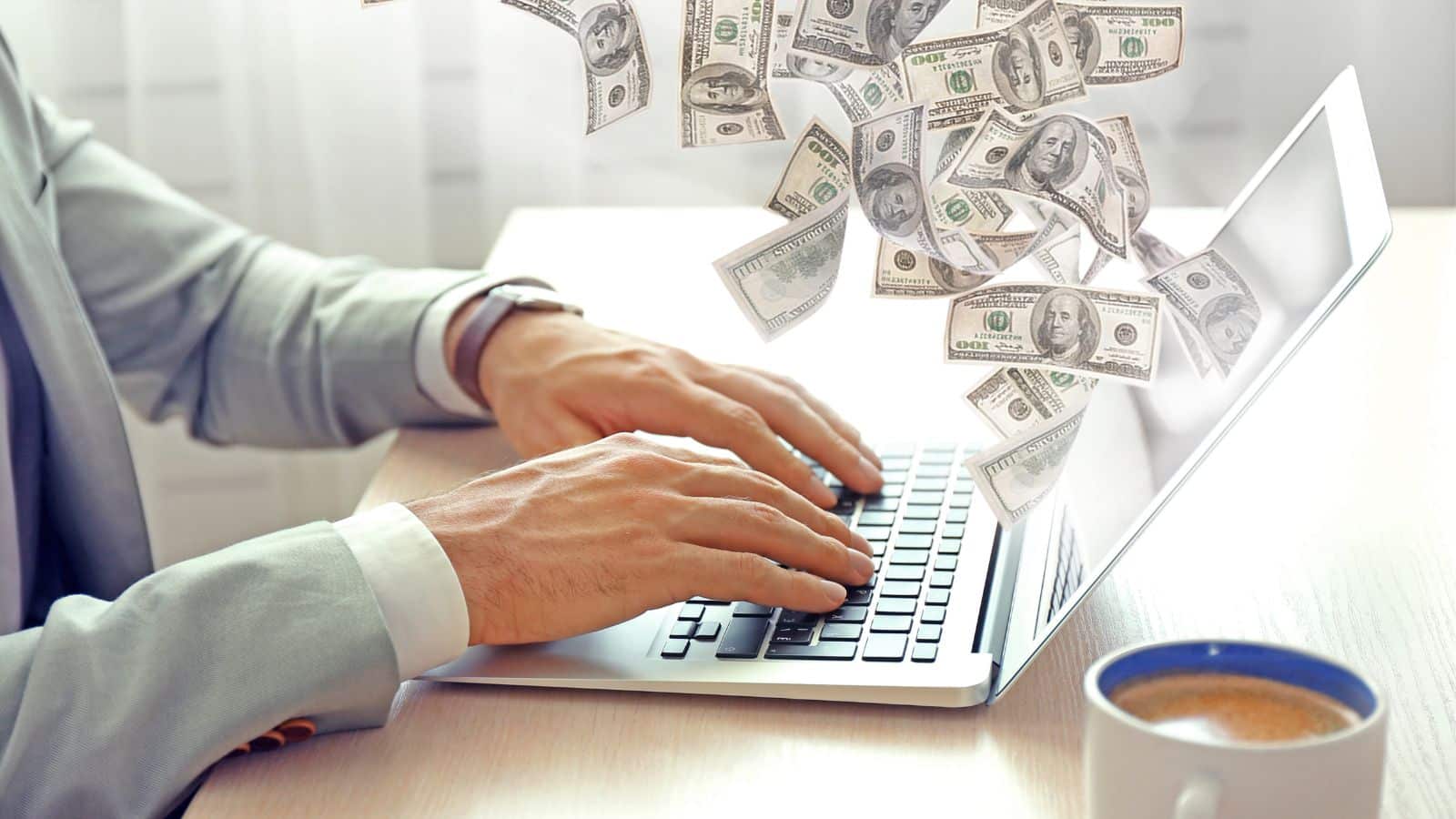 Person using laptop with money flying out of it
