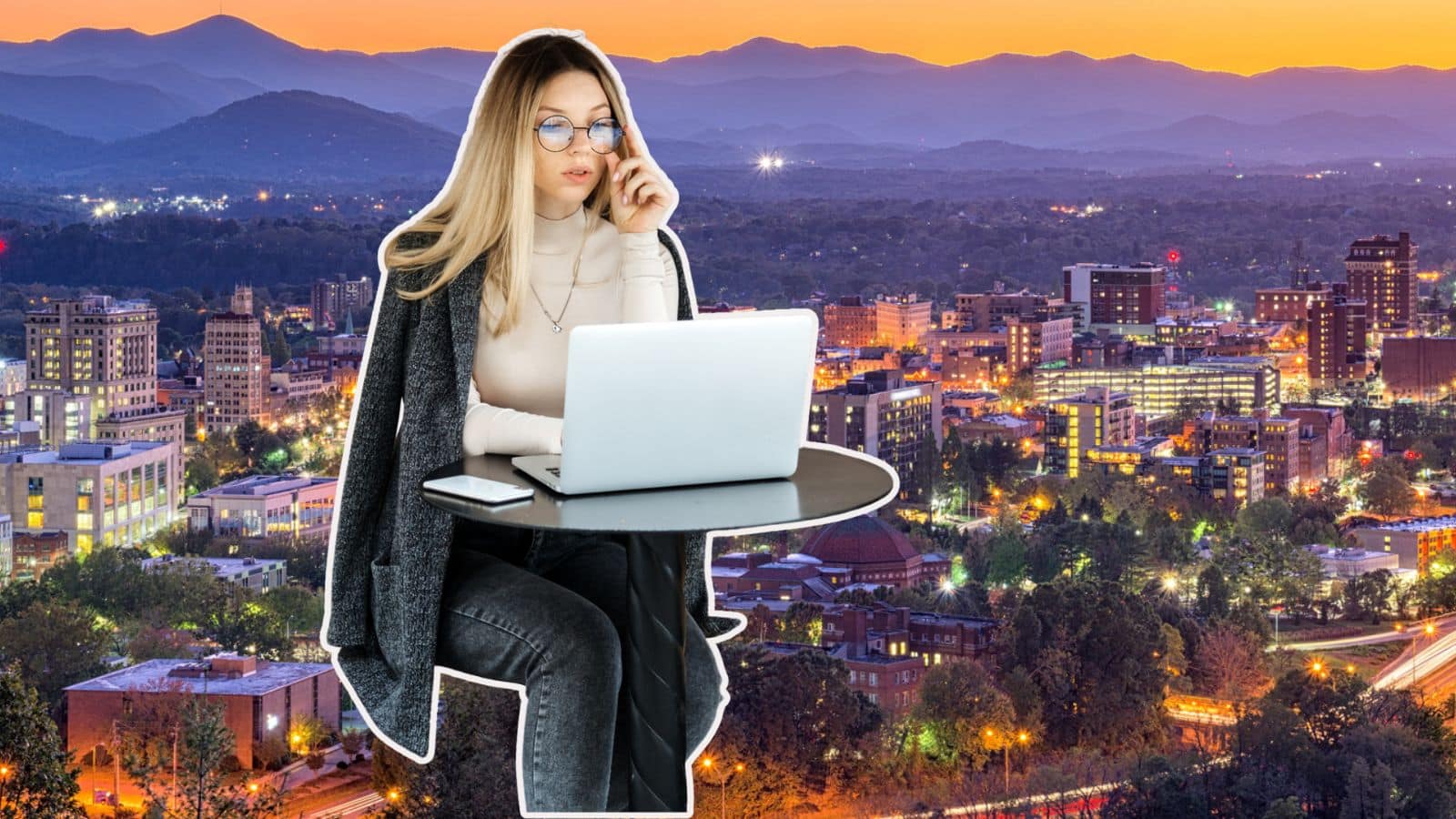 Young woman working remotely at a small table with a laptop over a skyline view of Asheville, NC