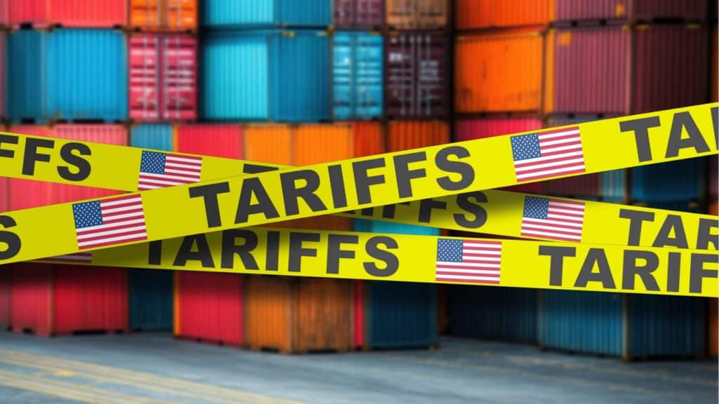 Shipping crates stacked high with yellow tape around them with an American flag and the word "tarrifs"