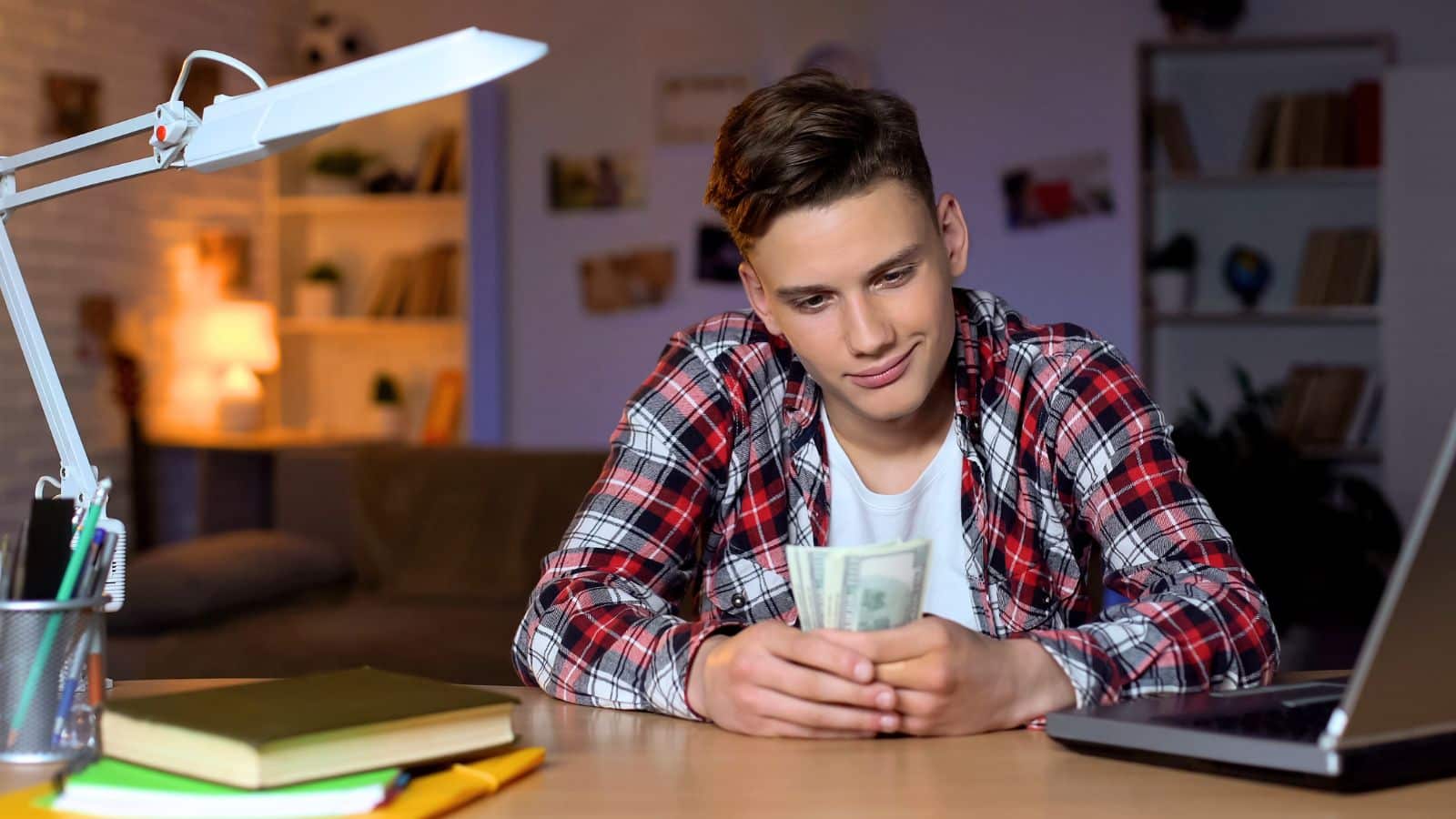 Teen boy sitting at his desk holding a bunch of money