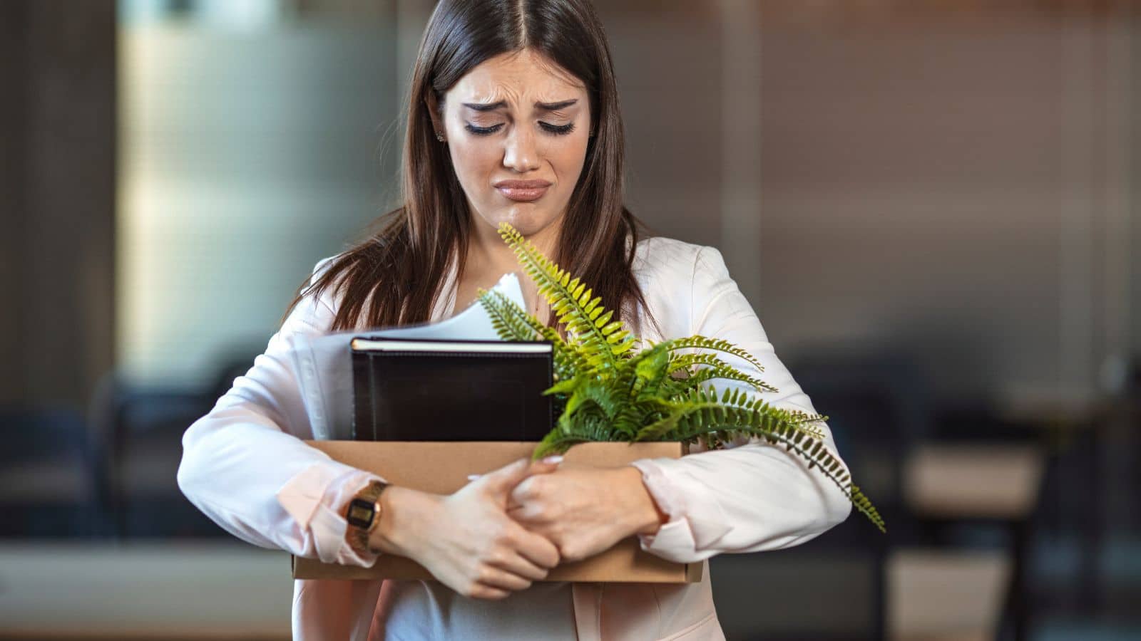 Young woman carrying a box of her belongings looking upset
