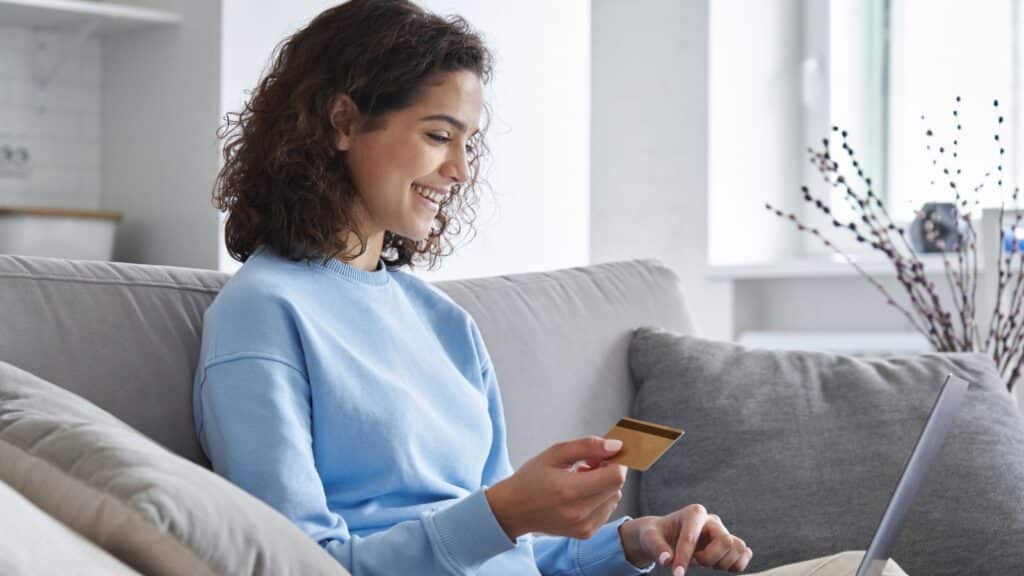 Young woman sitting on the couch and making a purchase on her laptop