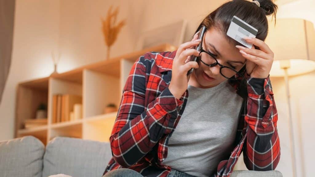 Young woman holding a credit card while talking on the phone and looking upset