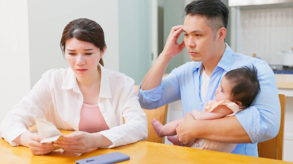 Couple holding baby and looking stressed over their finances