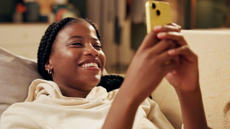 Happy Gen Z girl smiling and using her cell phone
