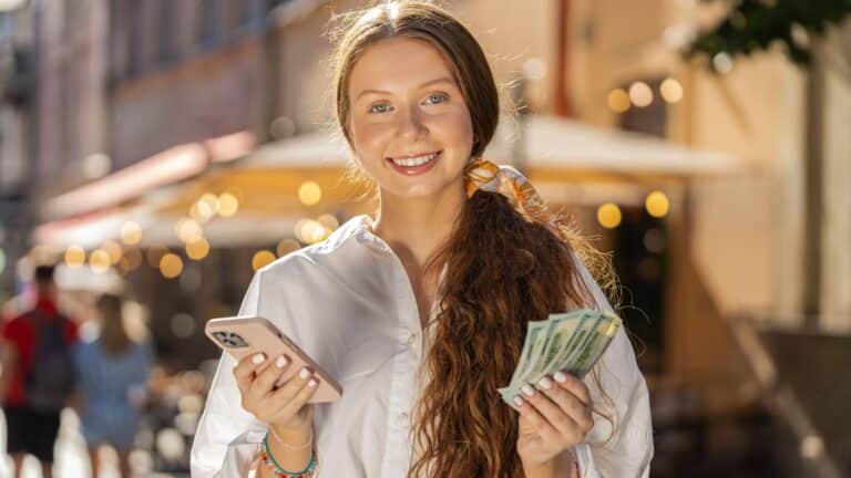 Teenage girl smiling and holding money and a call phone