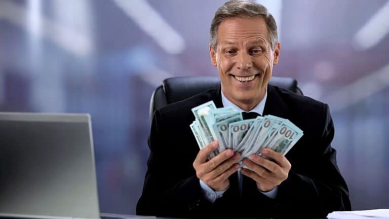 Greedy businessman sitting at his desk holding a bunch of cash