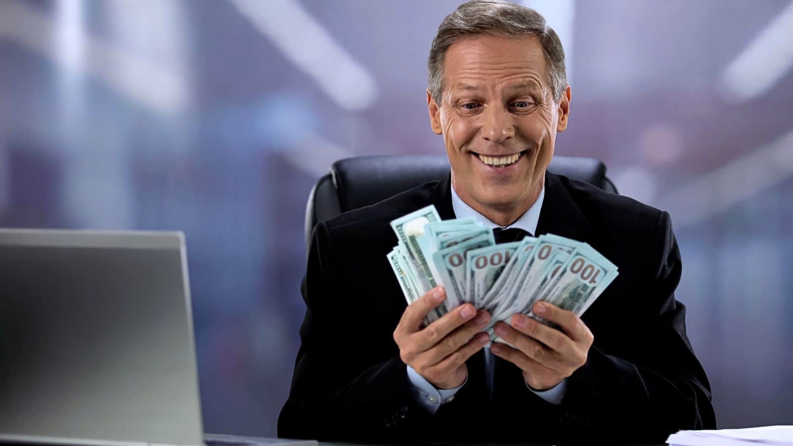 Greedy businessman sitting at his desk holding a bunch of cash