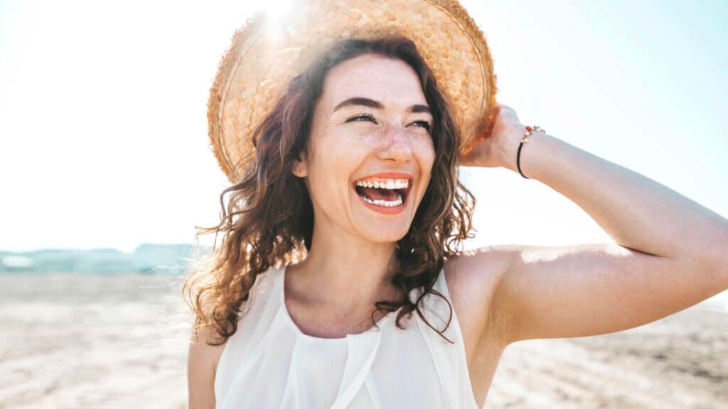 Happy woman wearing a hat smiling on the beach