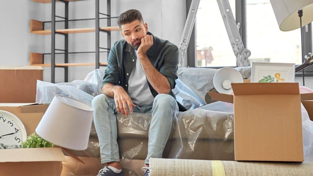 Man sitting on the couch looking sad as he's packing