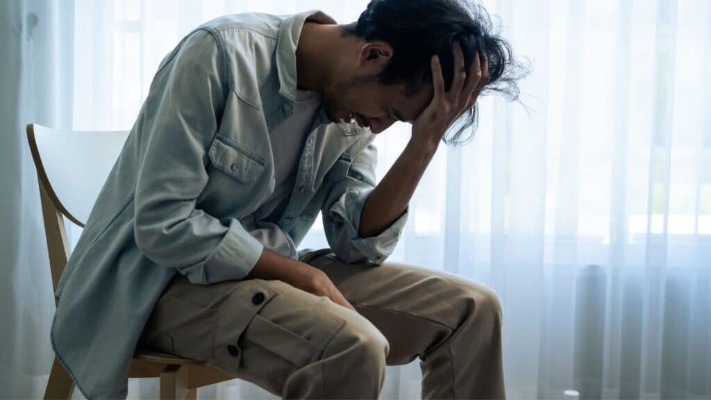 Man sitting in a chair leaning over looking stressed and upset