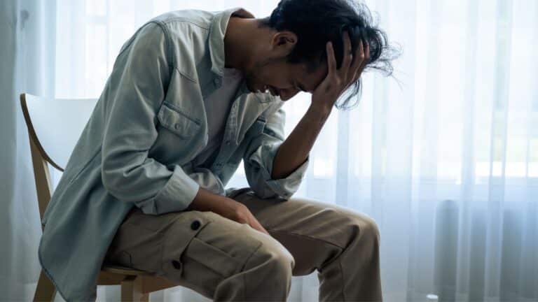 Man sitting in a chair leaning over looking stressed and upset