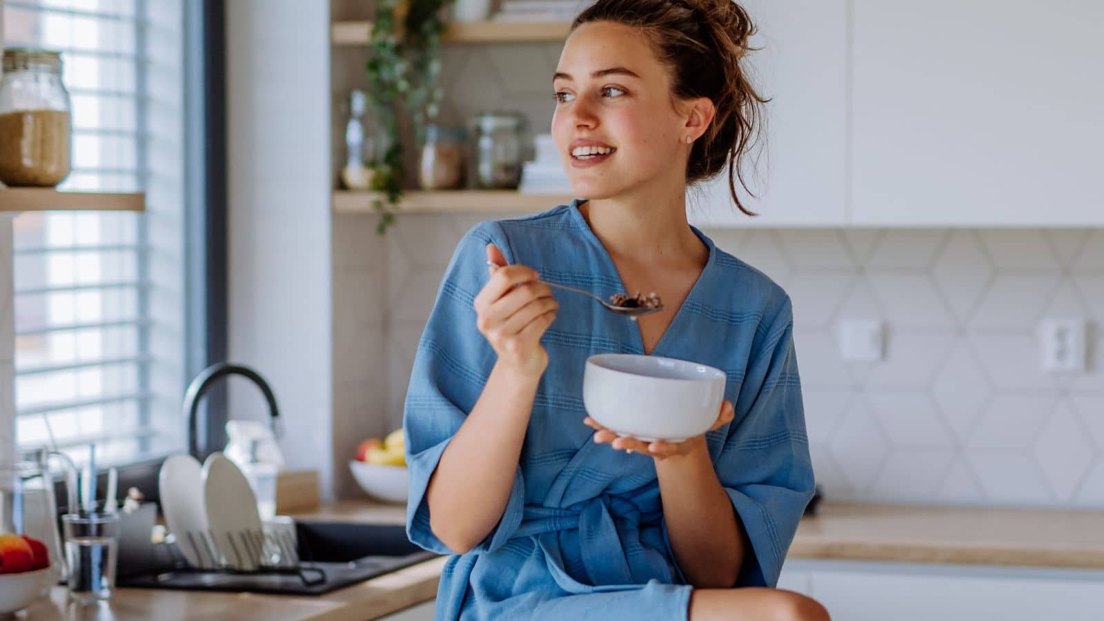 Woman sitting on counter eating a bowl of soup