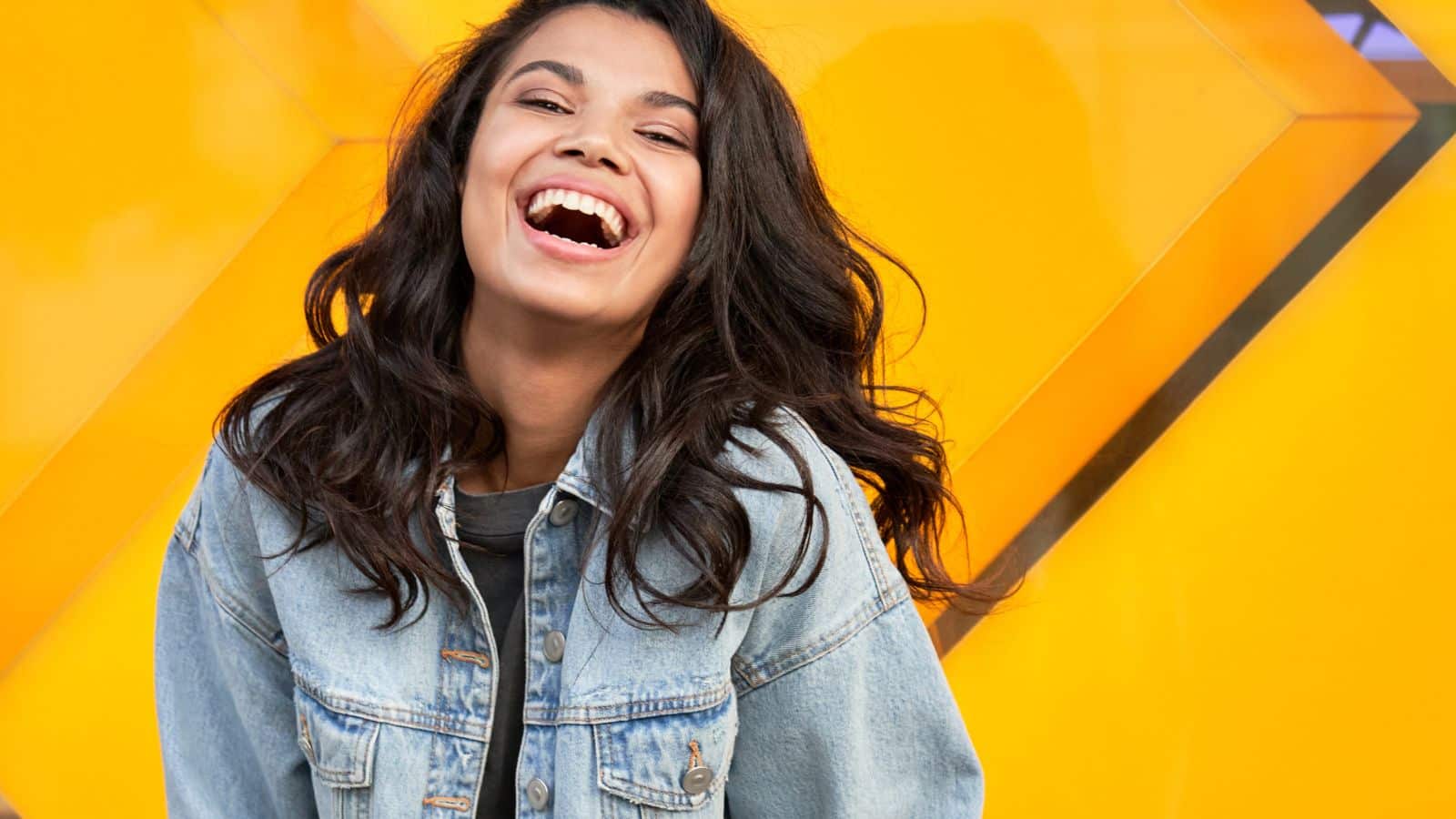 Young happy woman smiling in front of a bright yellow wall