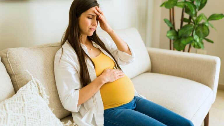 Pregnant woman sitting on the couch looking upset and holding her belly