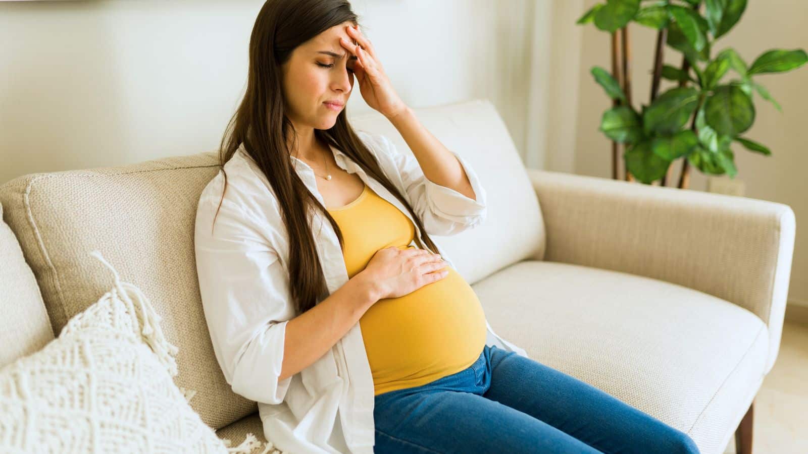 Pregnant woman sitting on the couch looking upset and holding her belly