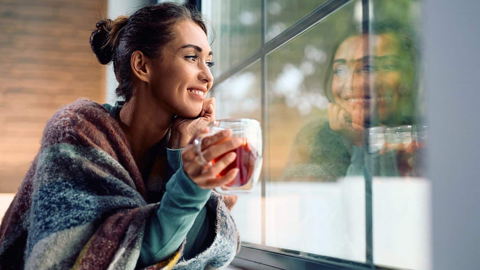 Young woman drinking tea and smiling while looking out the window