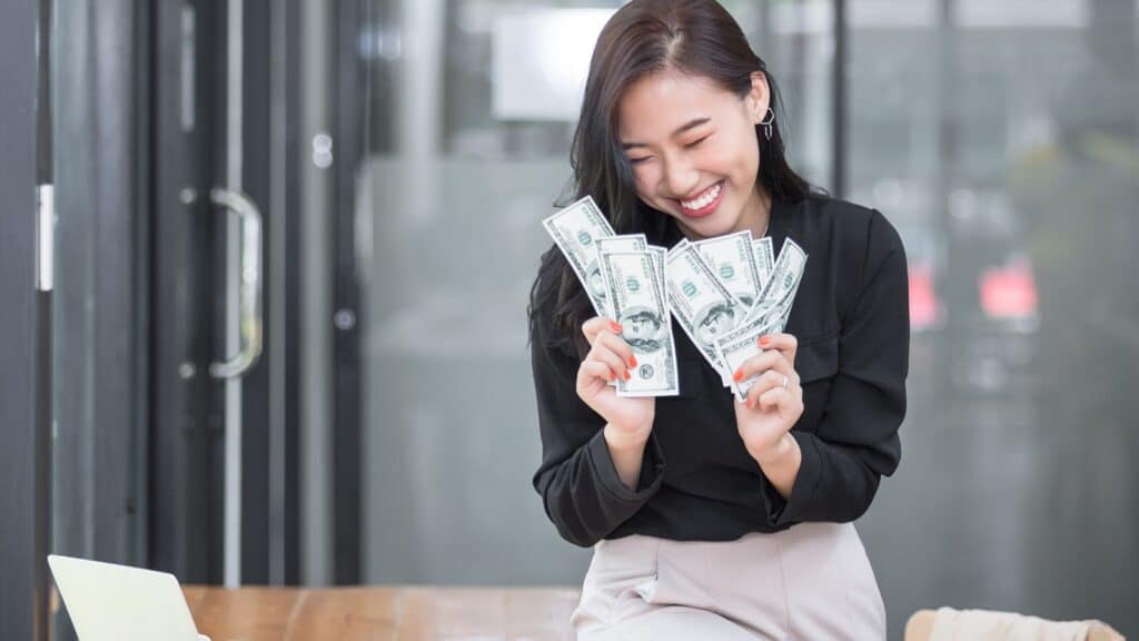 Young Asian woman sitting on a desk holding lot of cash