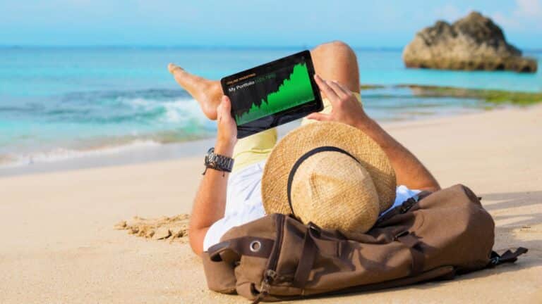 Man relaxing on the beach looking at his investments on a tablet