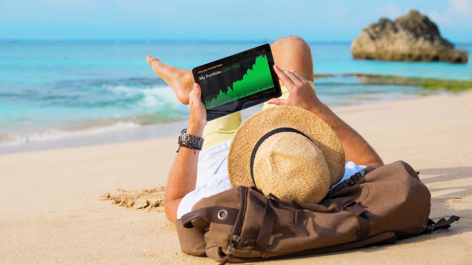 Man relaxing on the beach looking at his investments on a tablet