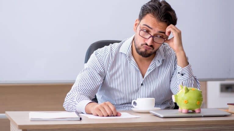 Man sitting at desk with coffee and a piggy bank