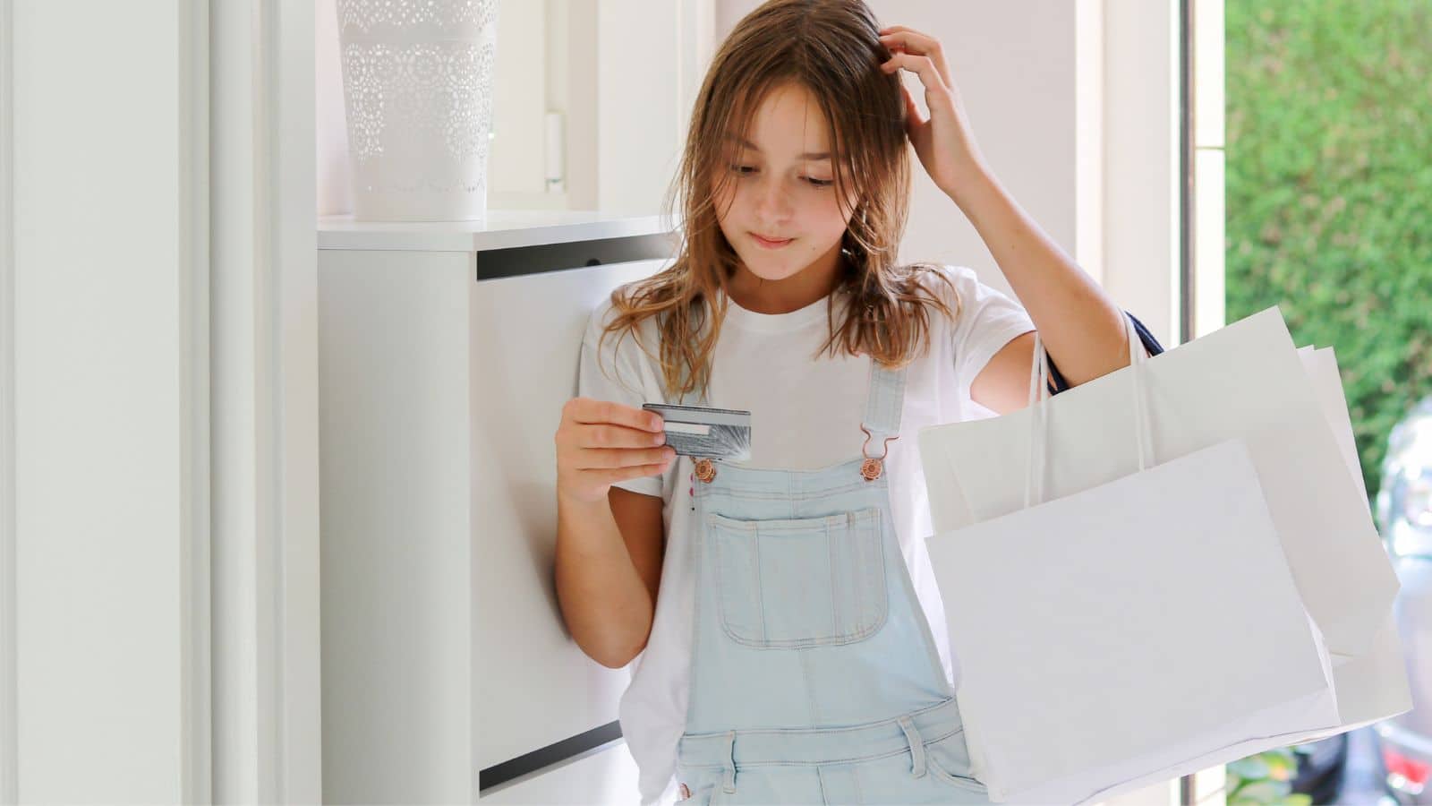 Young woman holding shopping bags and looking at her credit card with sadness