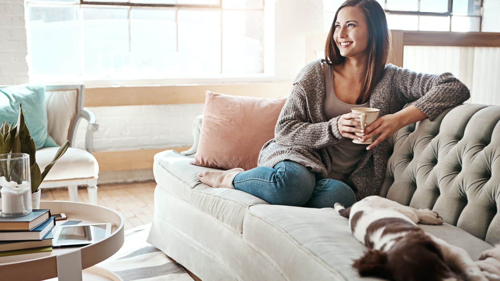 Woman sitting on the couch with her dog drinking coffee
