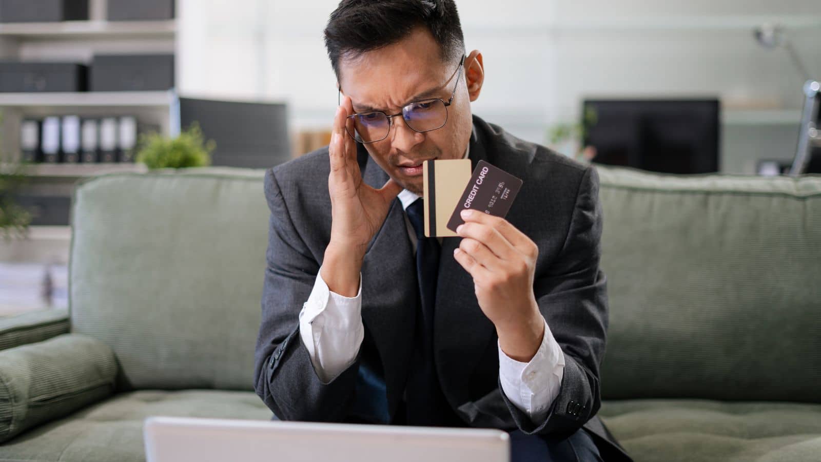 Man looking at his laptop stressed and holding credit cards