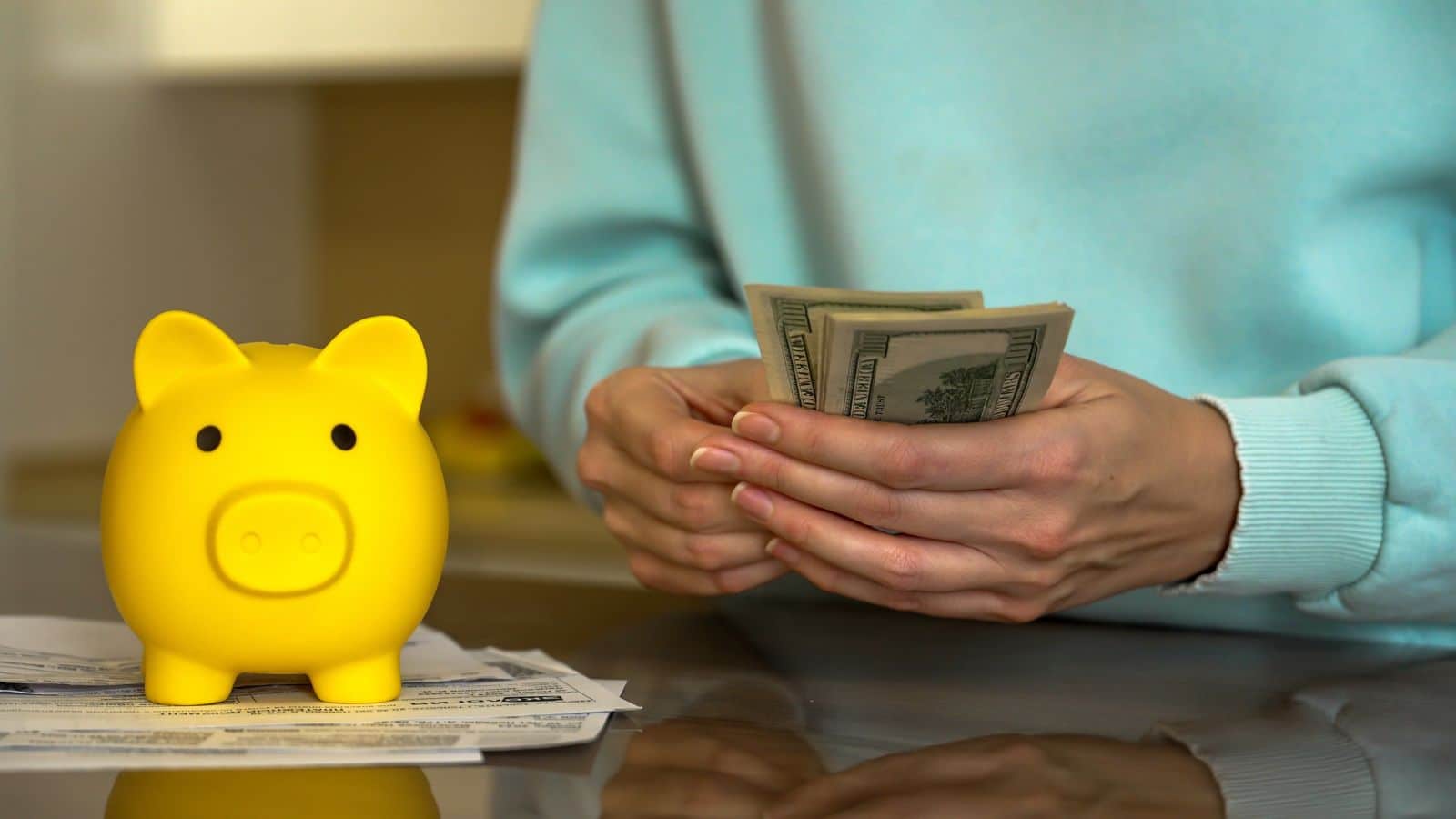 Woman holding cash with a yellow piggy bank on the table