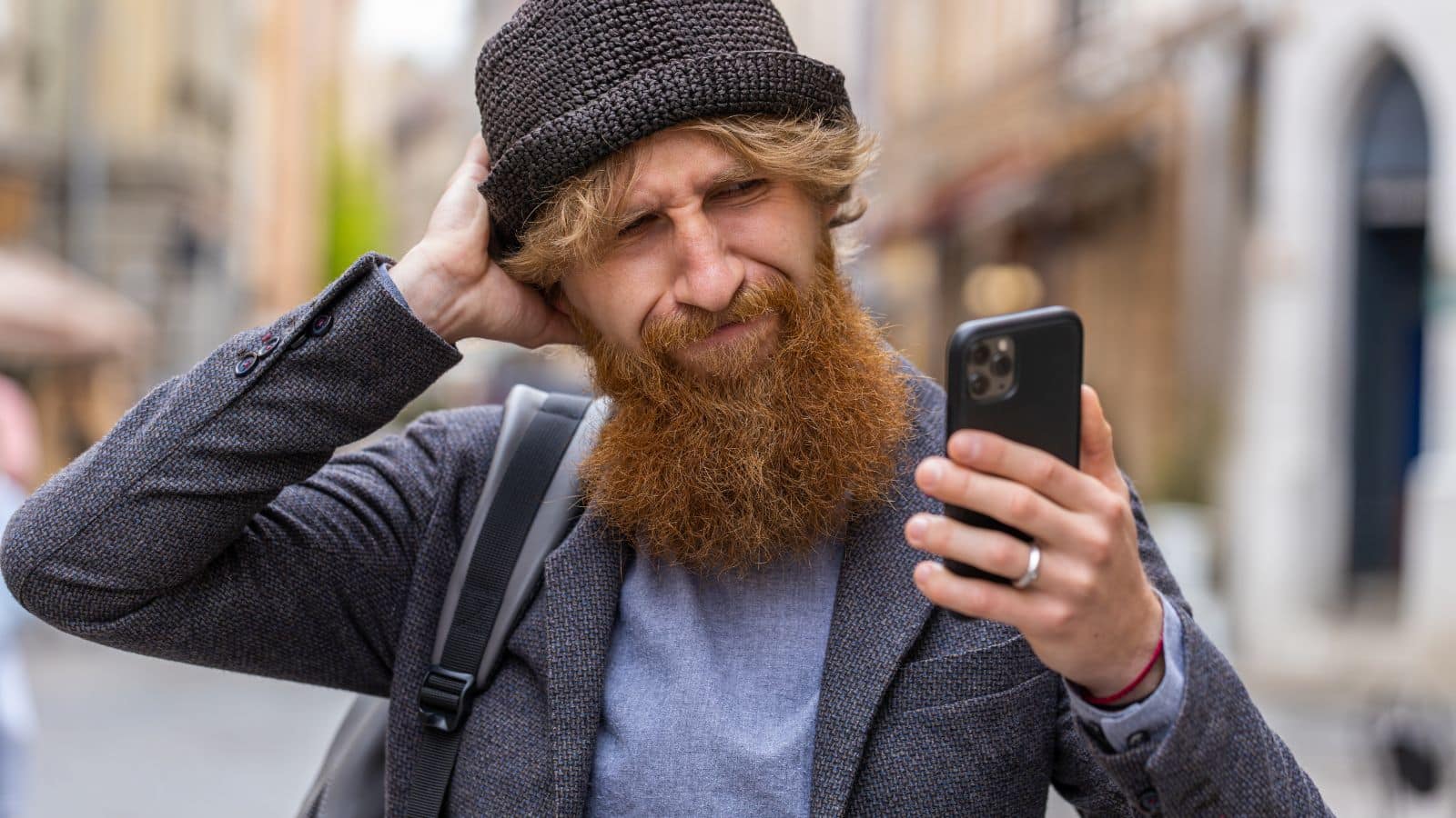 Man wearing a beanie, looking at his phone and looking confused