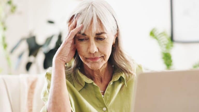 Older woman sitting at laptop looking very stressed