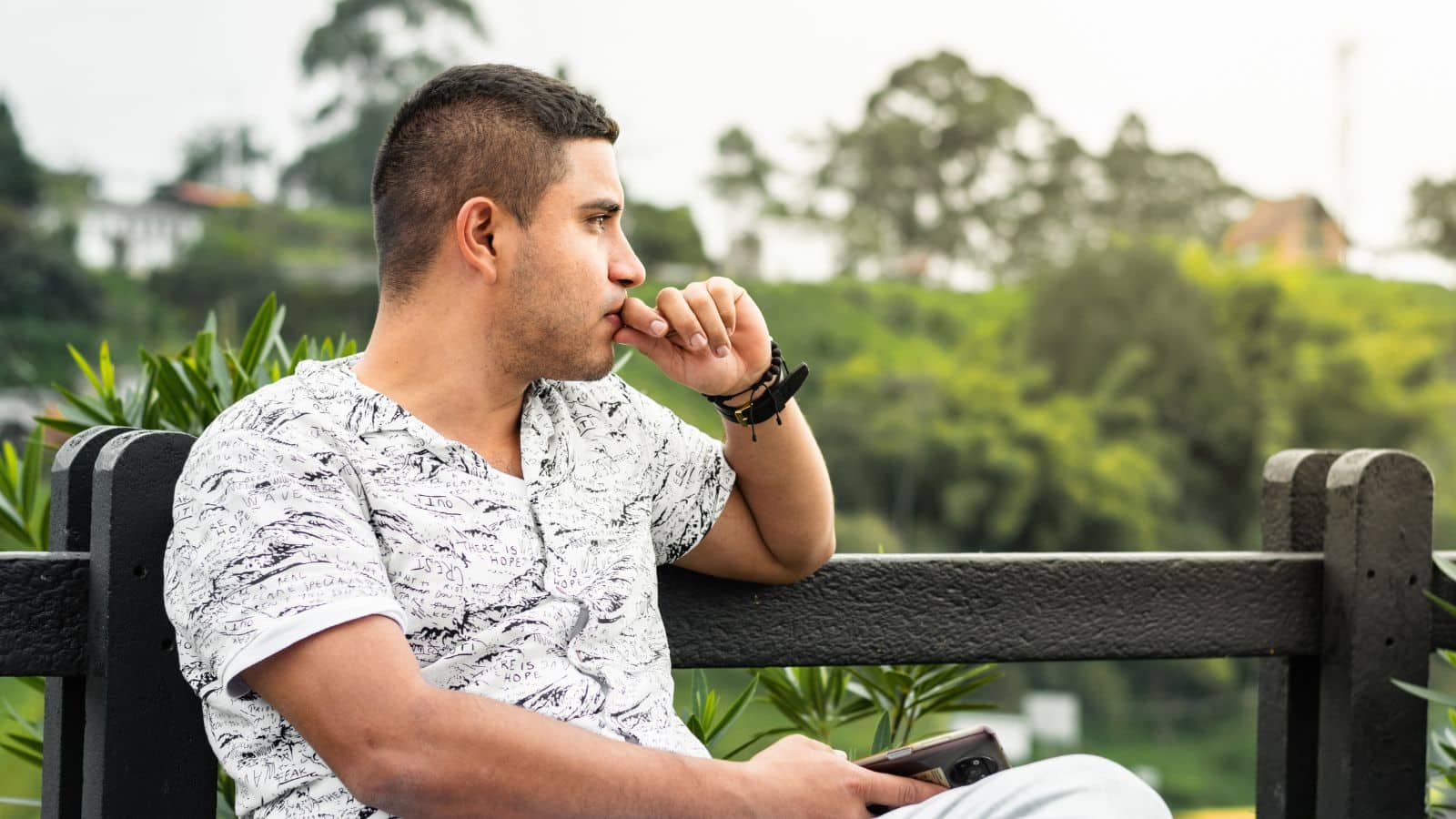 Young Latino man looking pensive sitting on a park bench