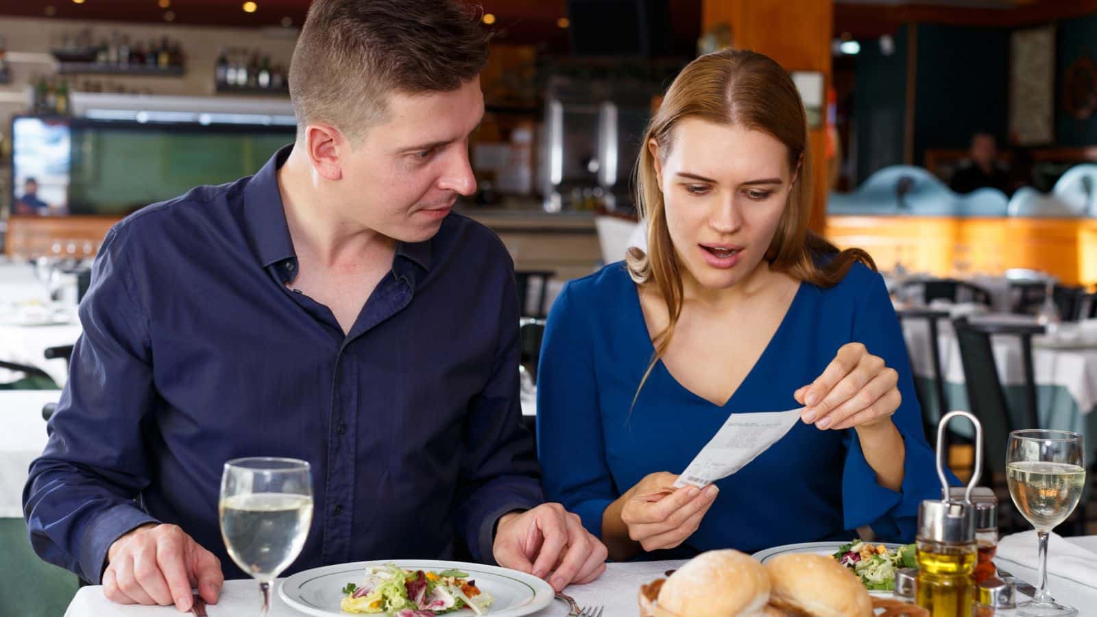 Couple at a restaurant looking shocked at their tab