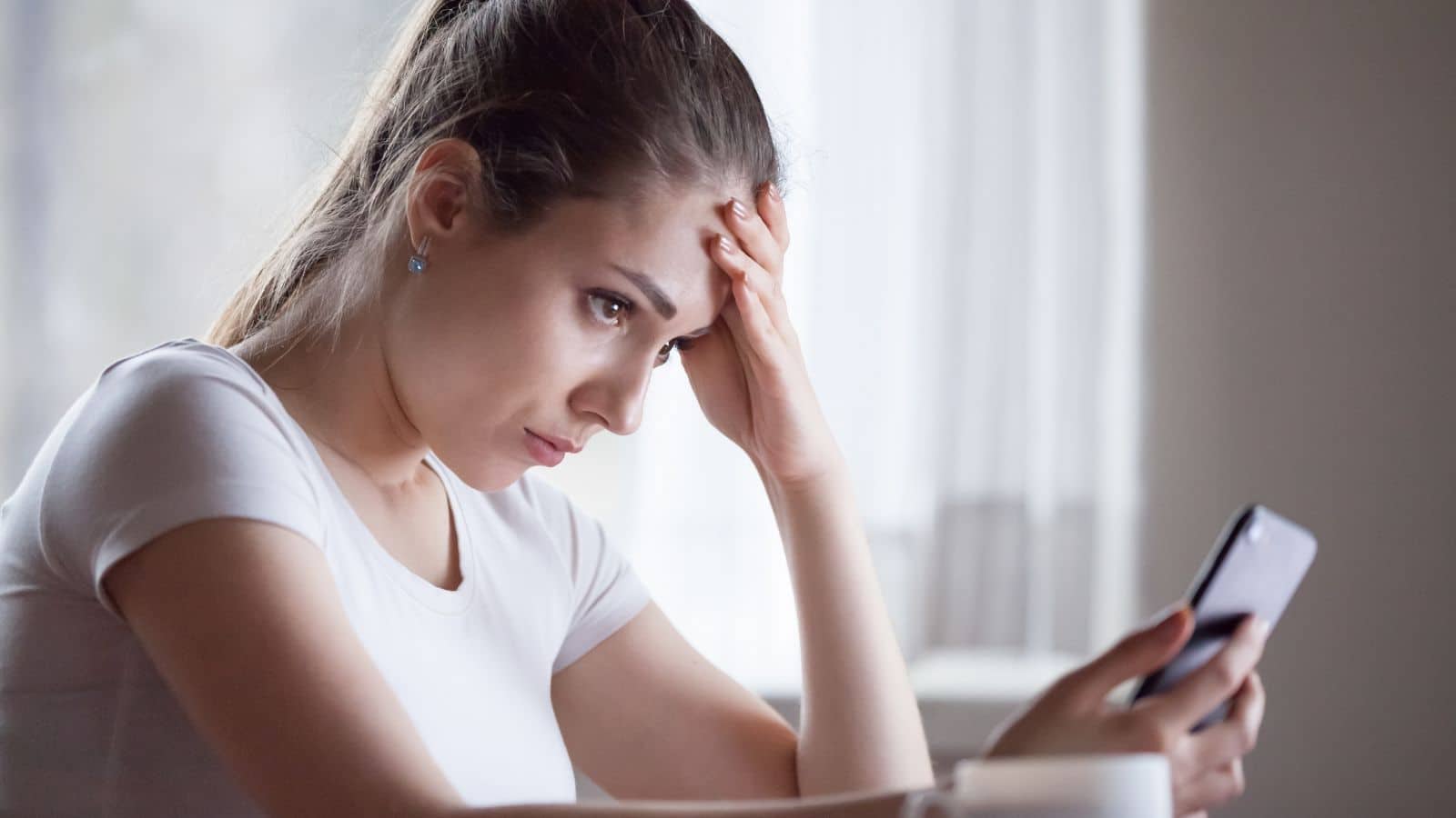 Woman looking down at her phone with a worried look on her face