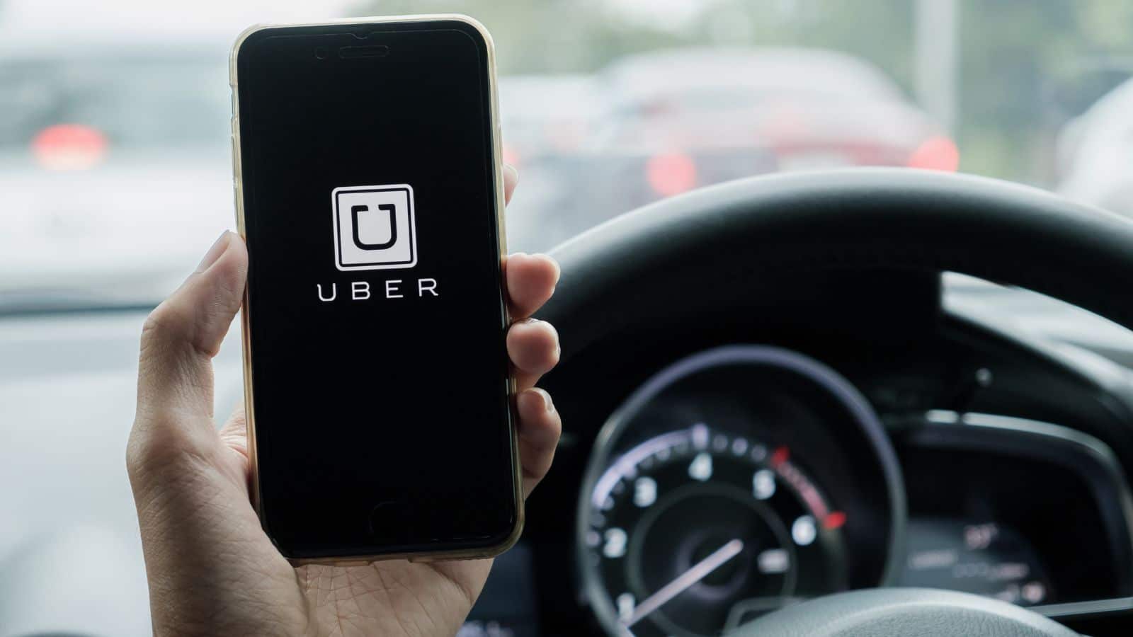 Man sitting in driver's side looking at the Uber app on his cellphone