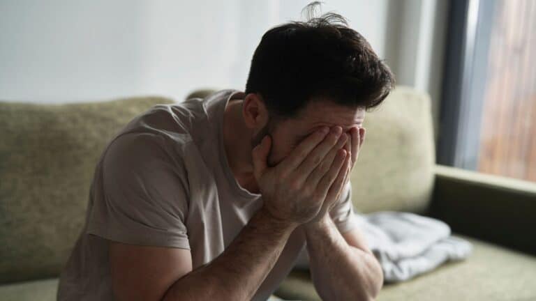 Man looking very upset sitting on the couch with his face in his hands