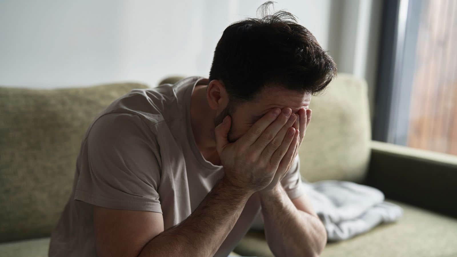 Man looking very upset sitting on the couch with his face in his hands