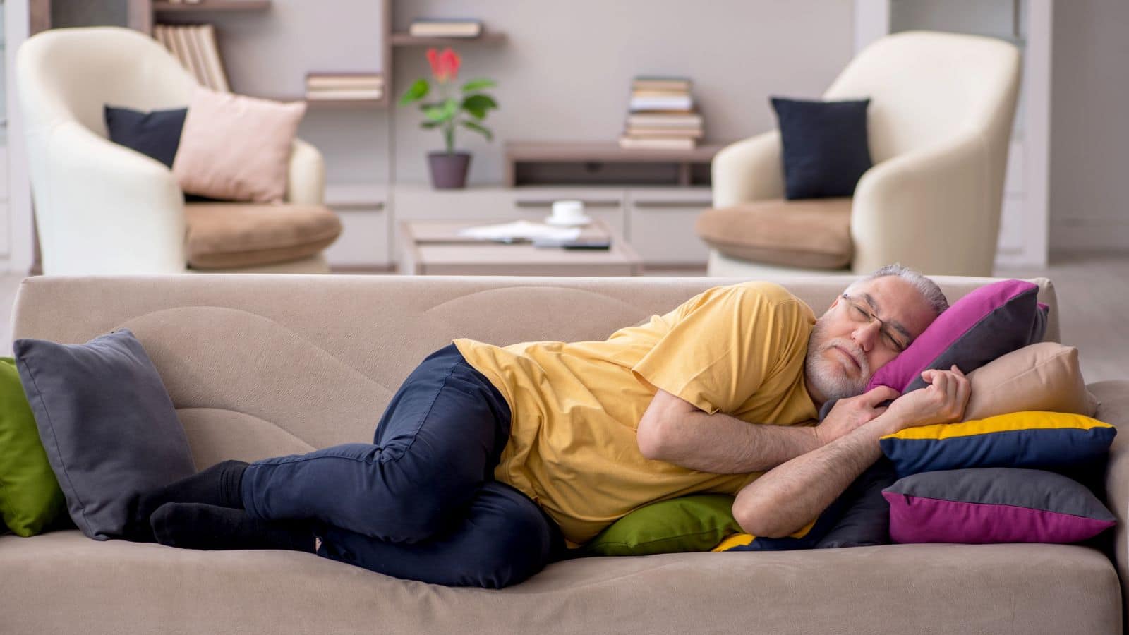 Older man sleeping on a couch with a bunch of pillows